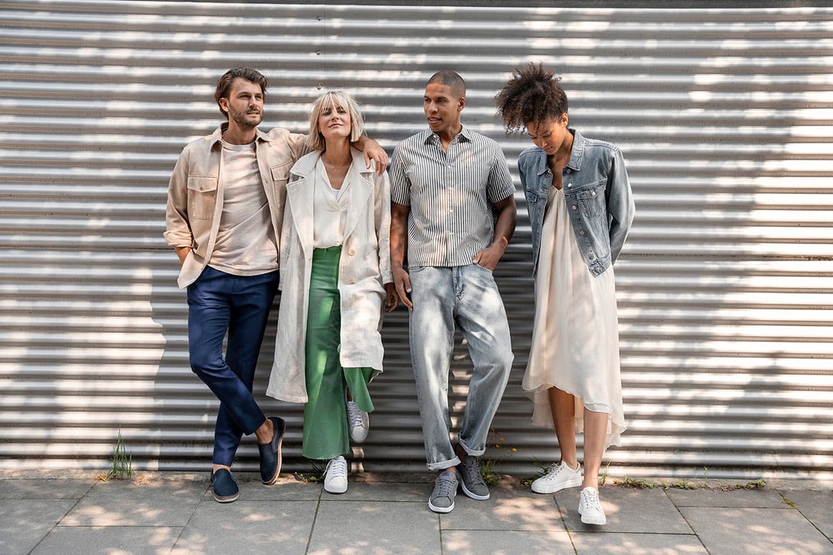 Vier Personen in Freizeitkleidung stehen entspannt vor einer Wellblechwand und genießen den sonnigen Tag.